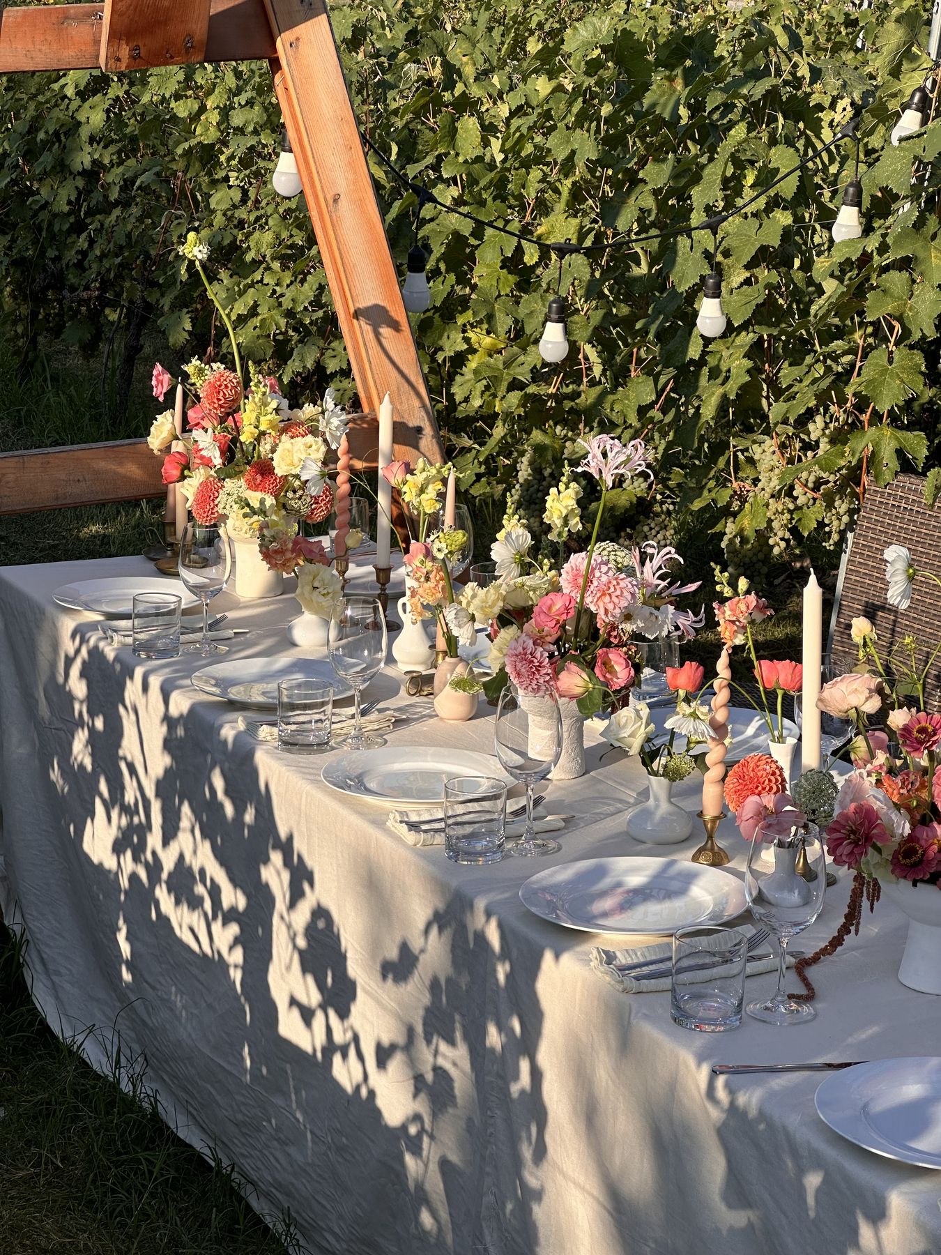 Garden dinner table with seasonal flowers and candles in dappled light